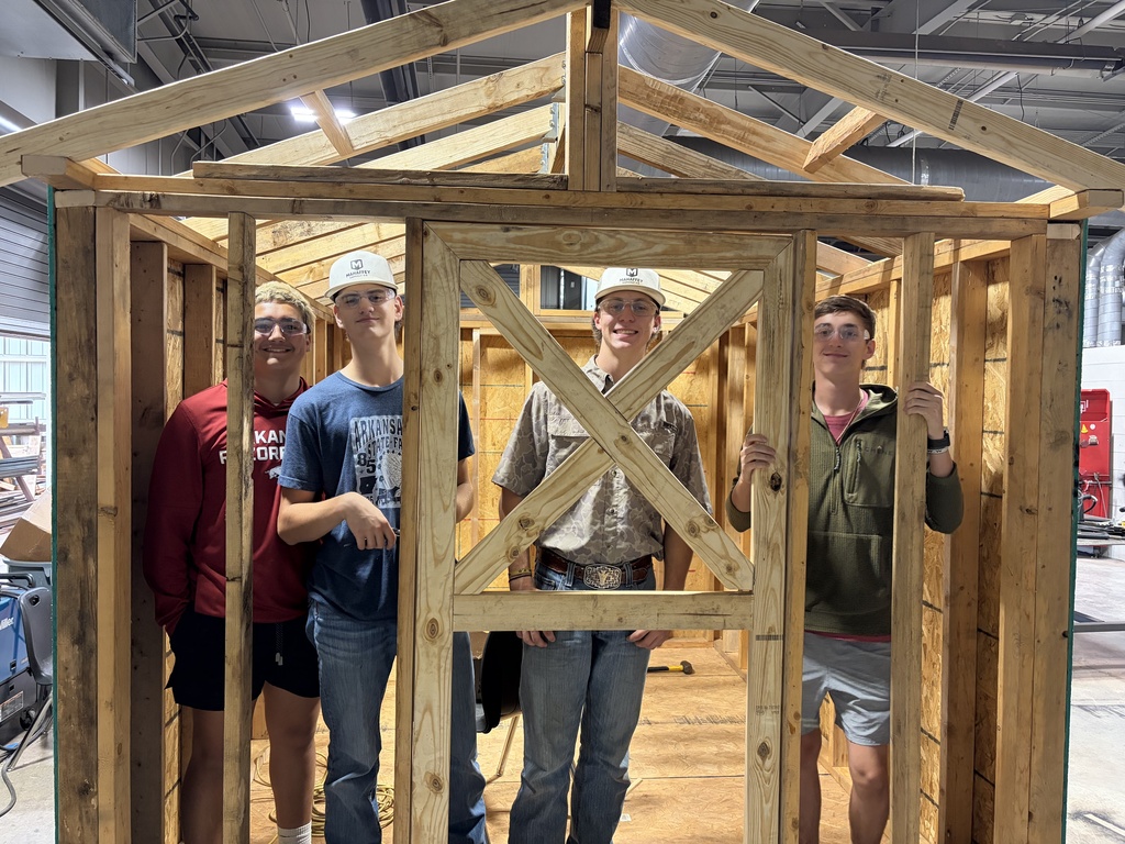 Four people in casual clothing stand inside a wooden frame of a structure under construction.