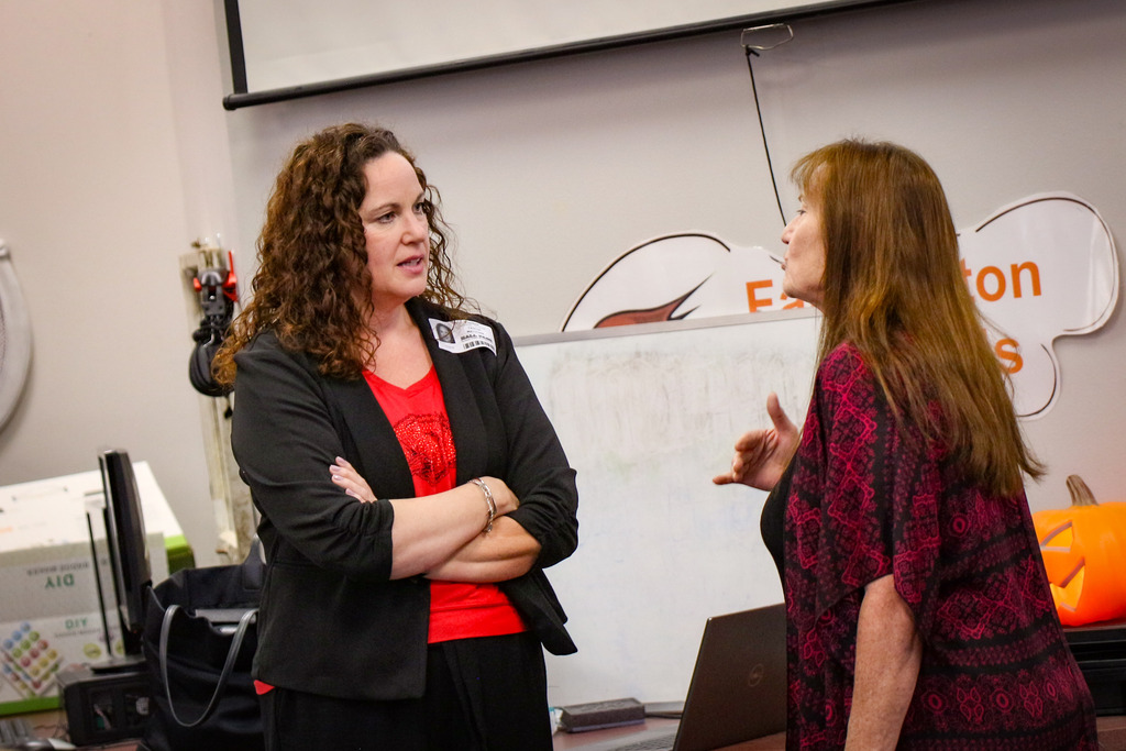 Two women face each other in a classroom, one with arms crossed, other with open mouth.