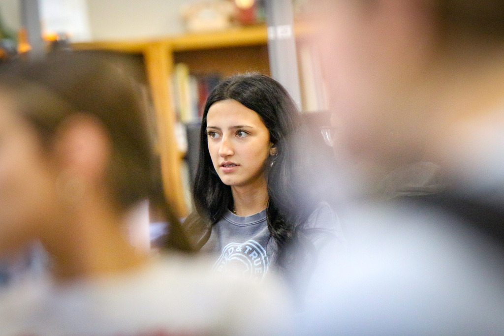 Woman with black hair standing in front of a group of students in a classroom.