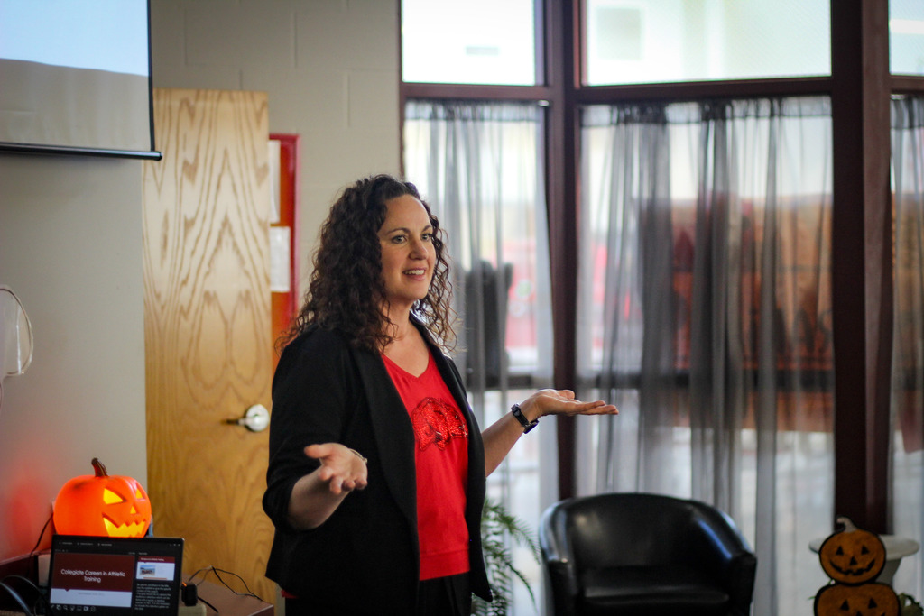 Woman standing in front of a room with a pumpkin on a table, gesturing with her hands.