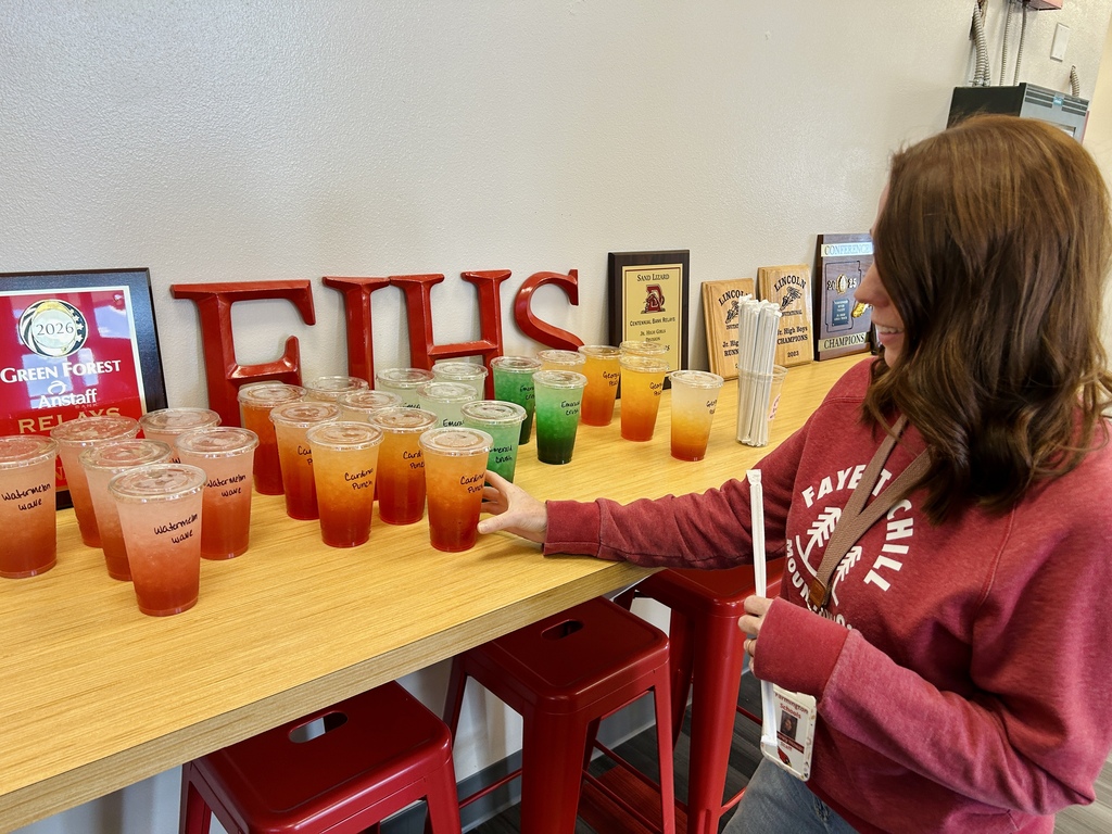 A woman with a backpack is picking up a cup with a straw from a table.