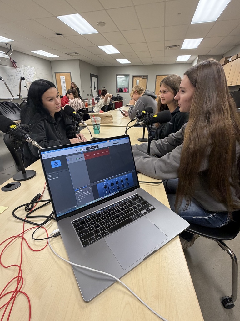 Four students sit around a table with laptops, wires, and microphones in front of them.