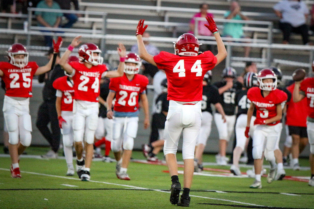 Young football players celebrating on a field, wearing red jerseys and helmets. Number 44 is raising both arms.