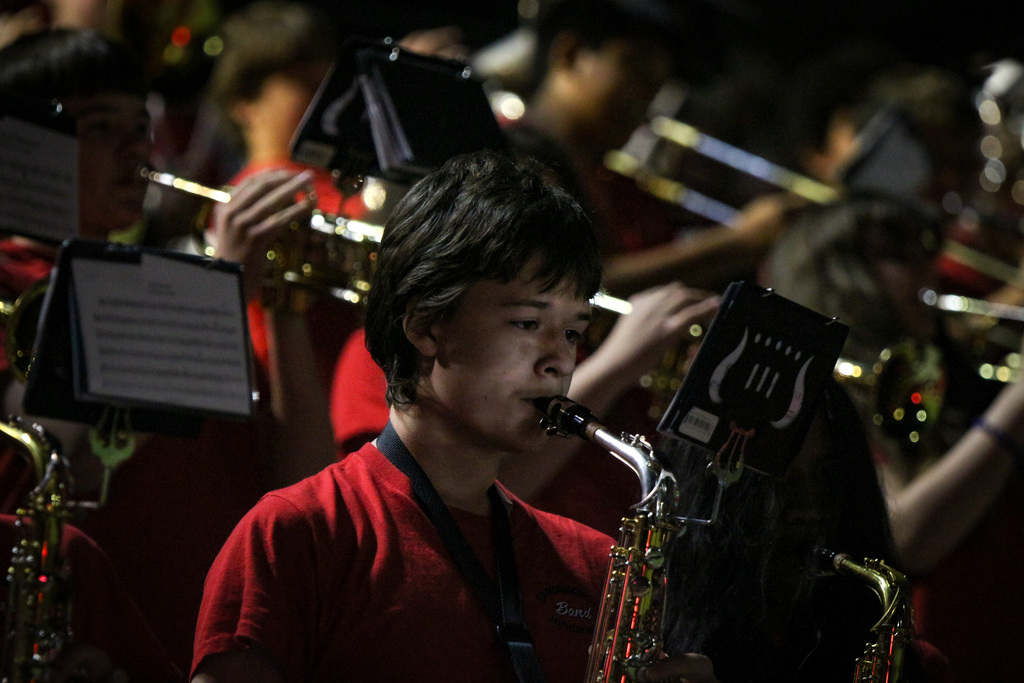 A student playing a saxophone while others play trumpets and trombones, all in red uniforms.