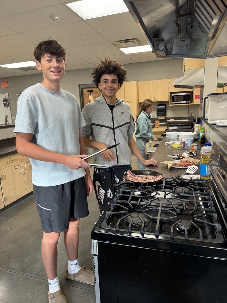Two young boys in a kitchen with a stove and countertop, one holding a pizza pan.