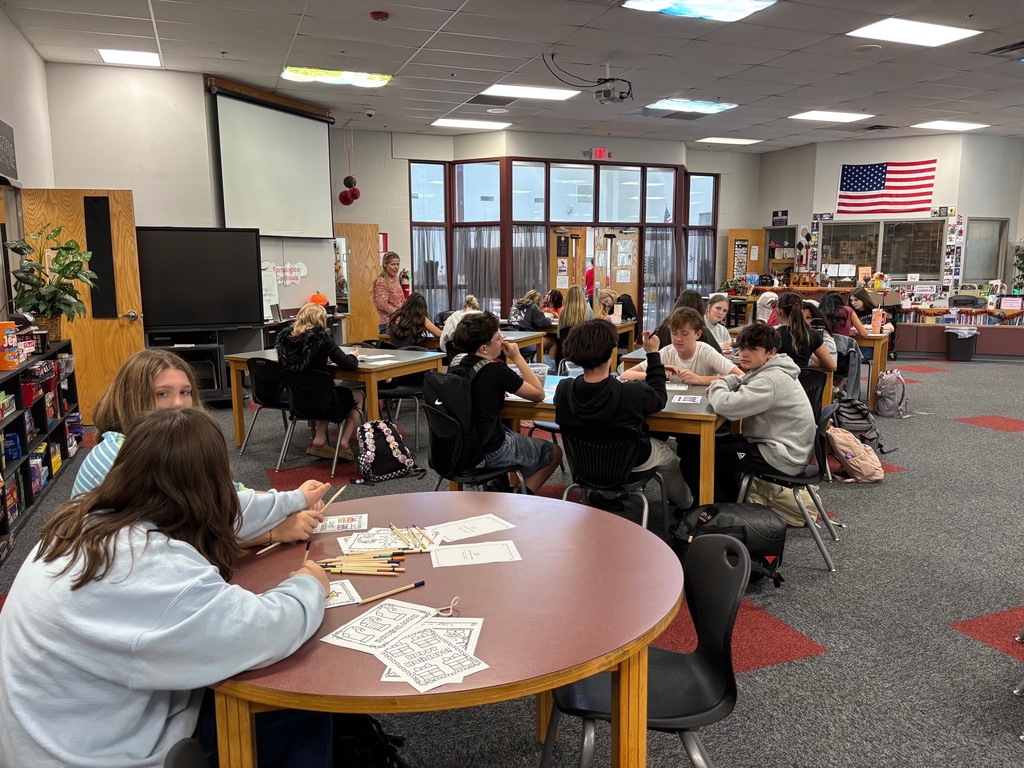 Classroom with students sitting at tables, one in a wheelchair, working with papers and pencils.