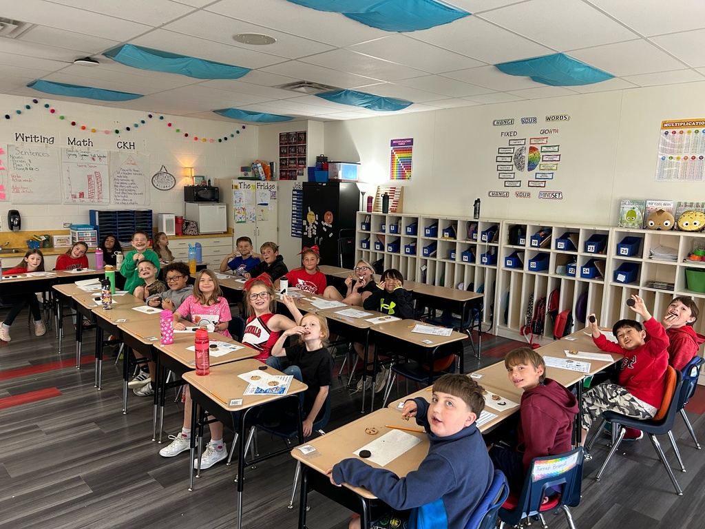 Classroom with students sitting at desks, some wearing jackets, a teacher, and whiteboards.