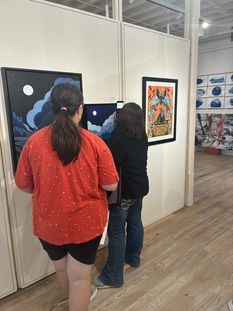 Two people view art in a gallery; one woman looks at a painting on the wall.