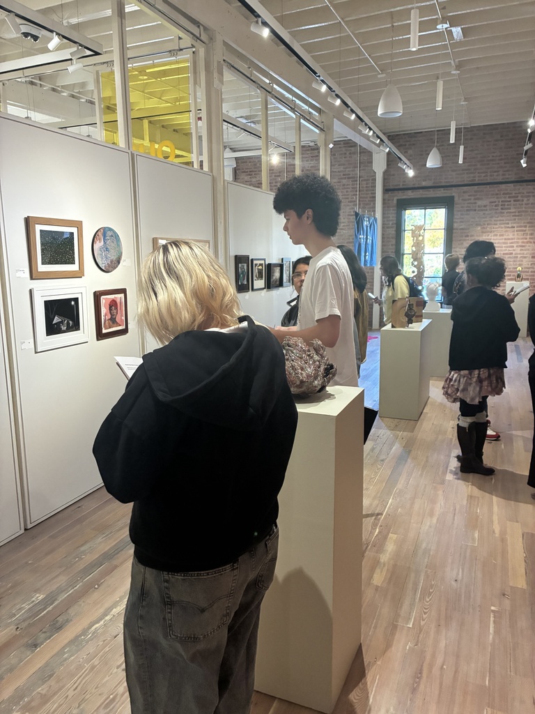 People in a room with art on walls, standing and looking at objects on display.