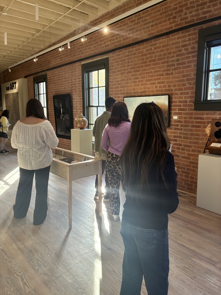 Five people in an indoor gallery. One woman looking at pottery on a table. Brick wall.