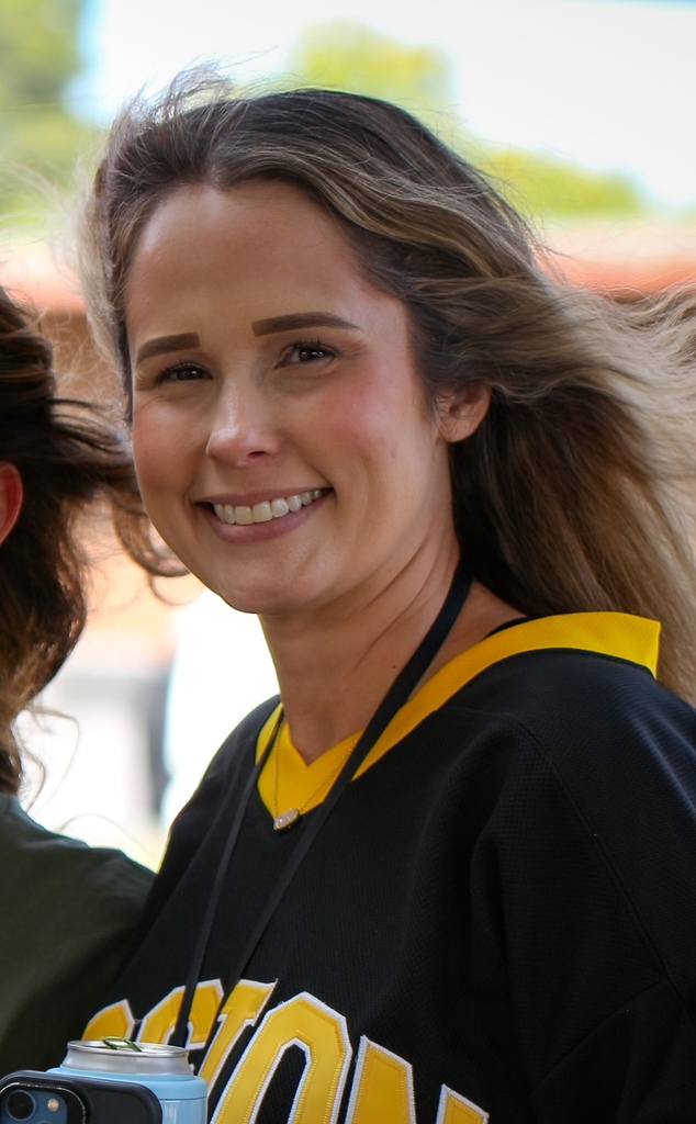 Woman with a ponytail smiling, wearing a sports jersey with yellow and black trim.
