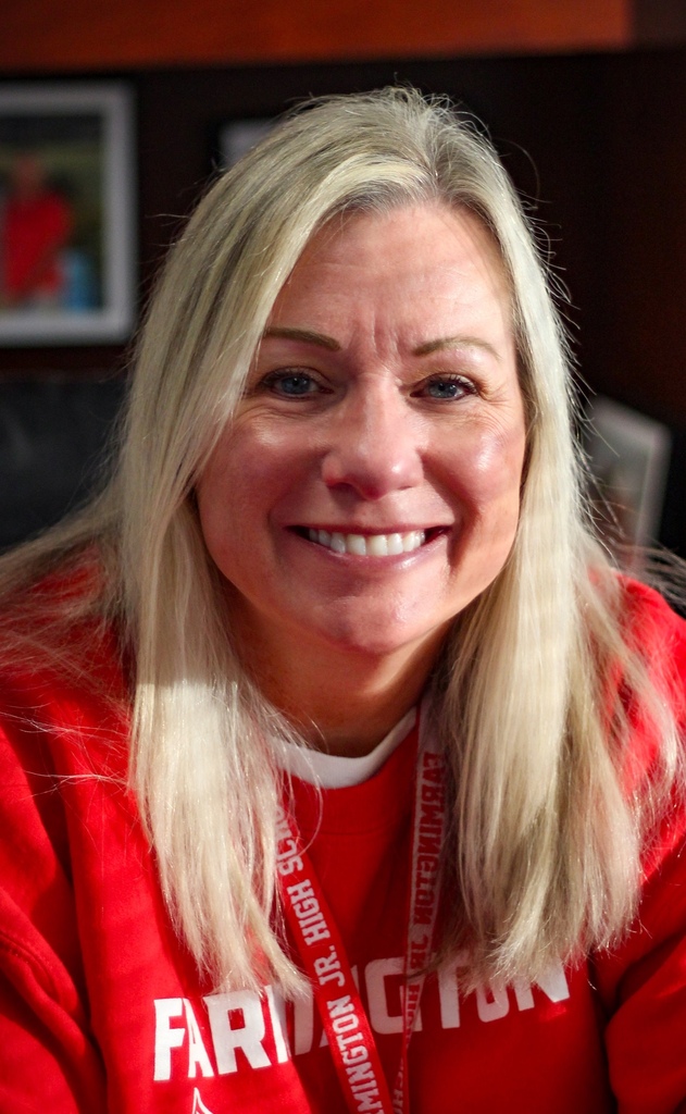 Woman with blonde hair wearing red sweatshirt with "FAIRMONT HIGH SCHOOL" printed on it, smiling.