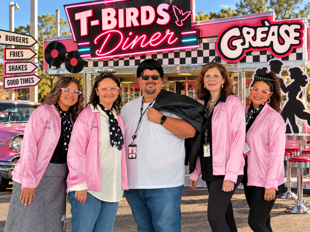 Five adults in pink jackets and lanyards standing in front of a diner sign with a checkered pattern.