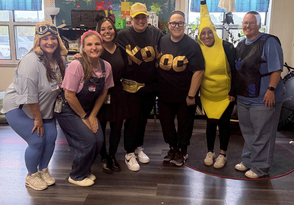 Group of people standing on wooden floor, some wearing costumes, posing for a photo.