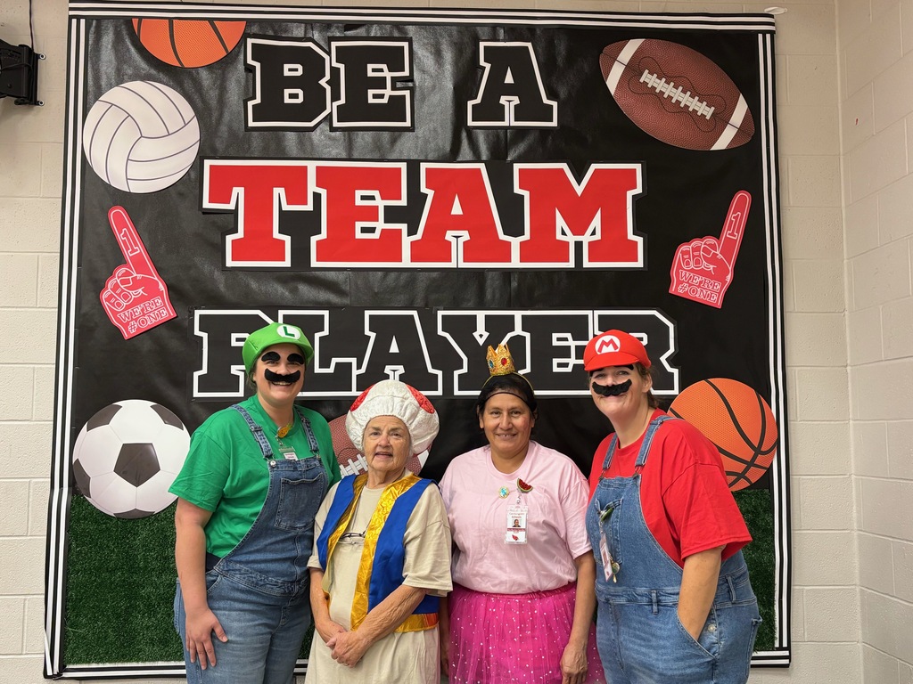 Four adults dressed in costumes, including chef's hats and a crown, pose in front of a banner.