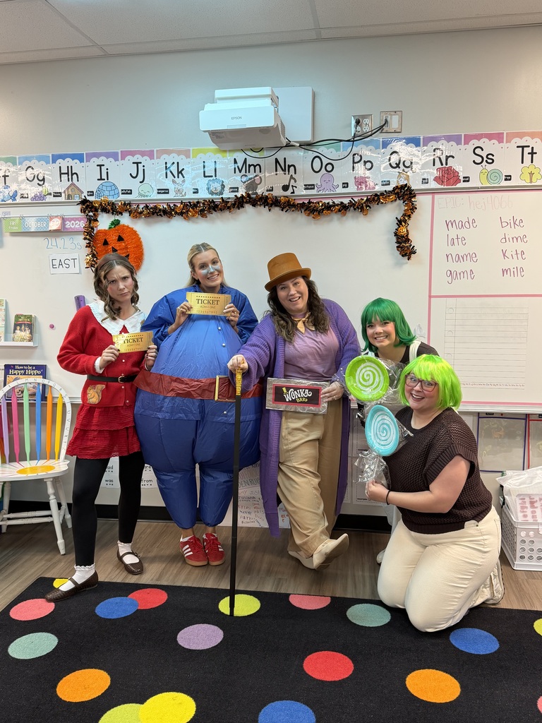 Five people in costumes pose in a classroom. One wears a red coat and holds a paper cup.