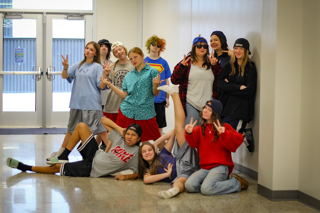 A group of students poses in a hallway, some kneeling, some standing, with a glass door behind them.