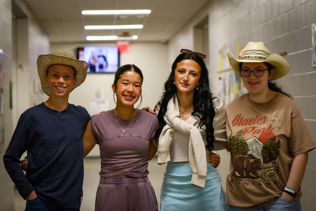 Four students in hats, standing together in a hallway. One wears a cowboy hat, another has a scarf.