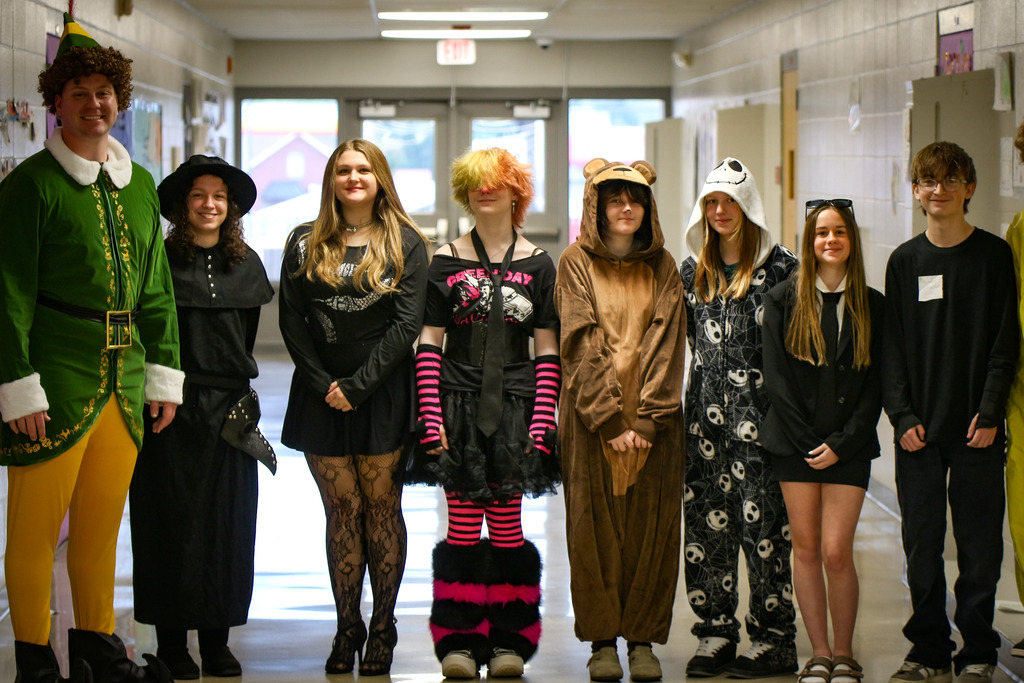 A group of students dressed in various costumes standing in a hallway, with lockers on either side.