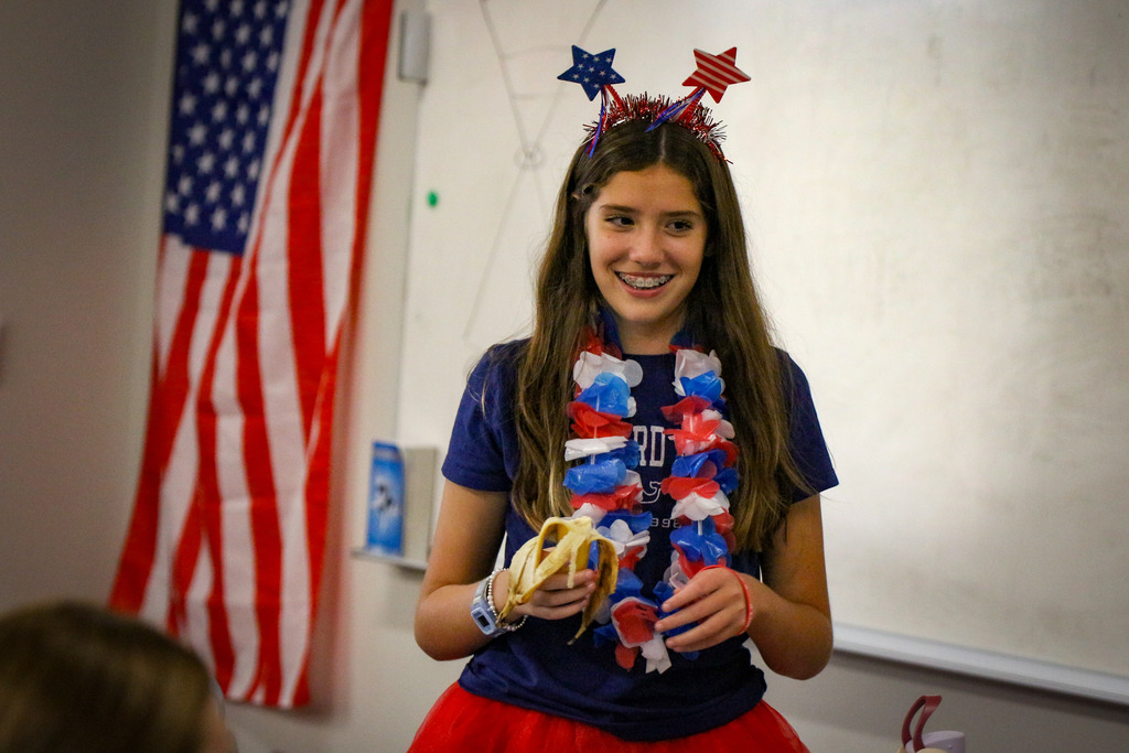 Girl wearing red, white and blue garland and a hat with stars, holding a banana.