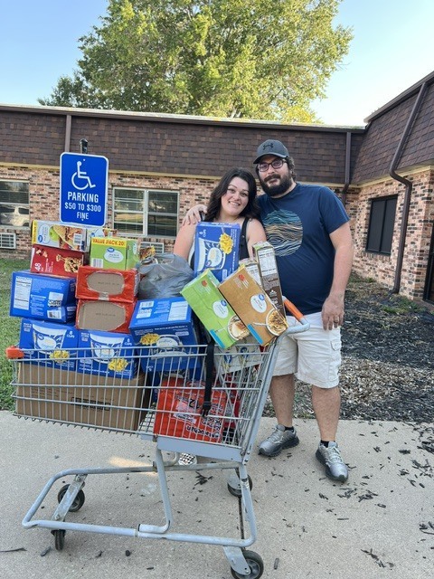 two people standing aside a grocery cart filled with groceries