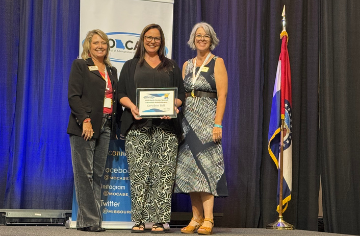 Three women on stage as one receives an award