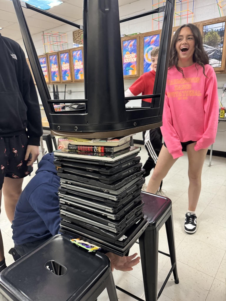 a weight bearing bridge holding up many chromebooks and an upside down chair with a student surprised and excited at the result