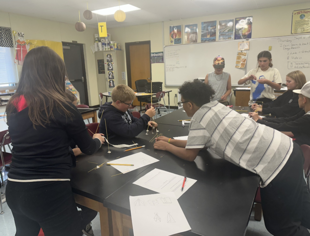 Students engaged in an engineering design challenge, building tall towers out of spaghetti and marshmallows while working in small teams.