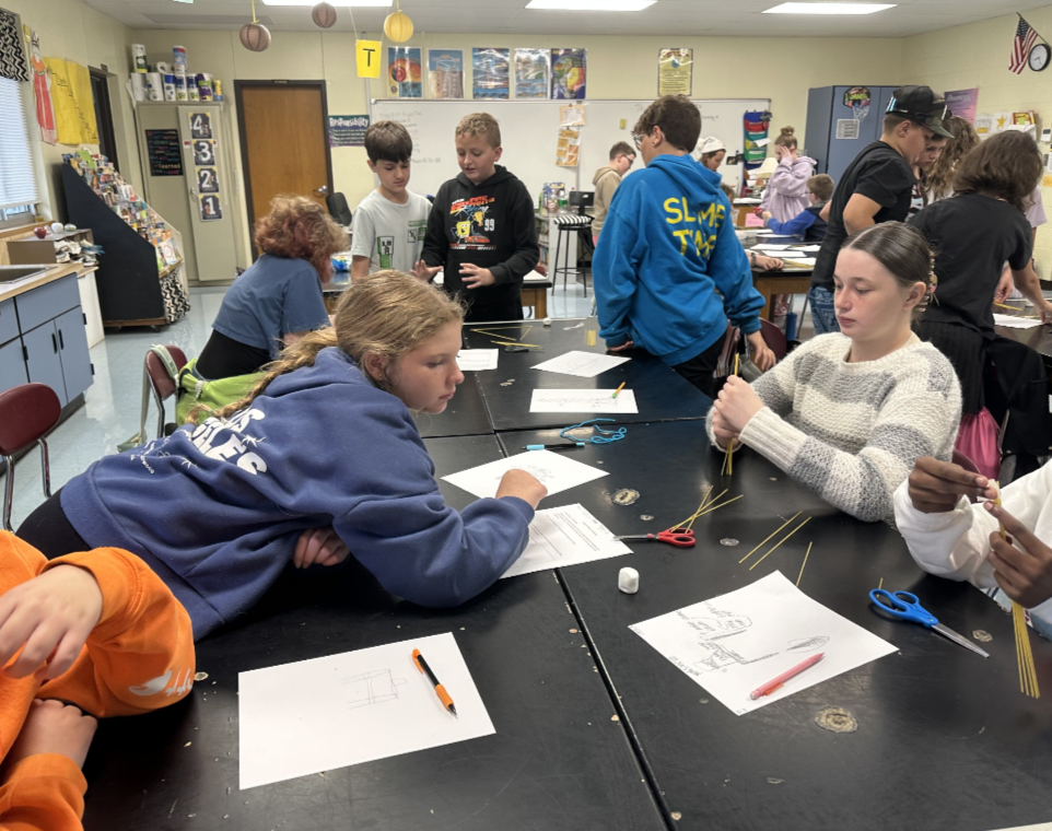 Students engaged in an engineering design challenge, building tall towers out of spaghetti and marshmallows while working in small teams.
