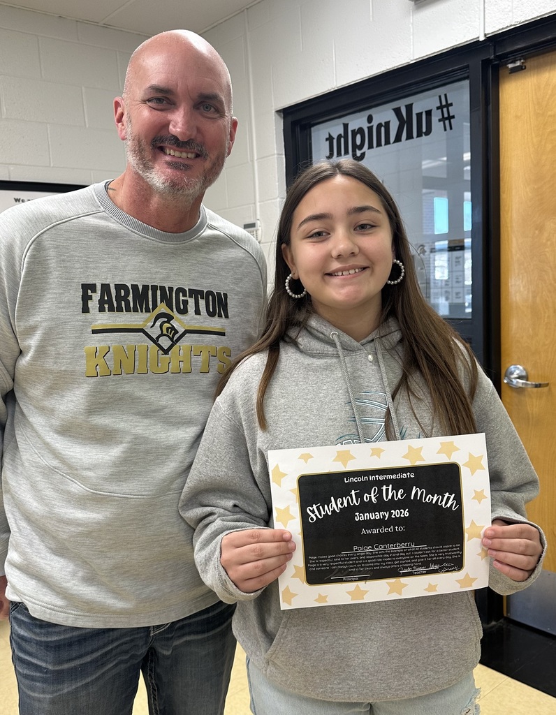 A student and a principal pose together for a celebratory photo. The student is smiling and holding an official "Student of the Month" award certificate.