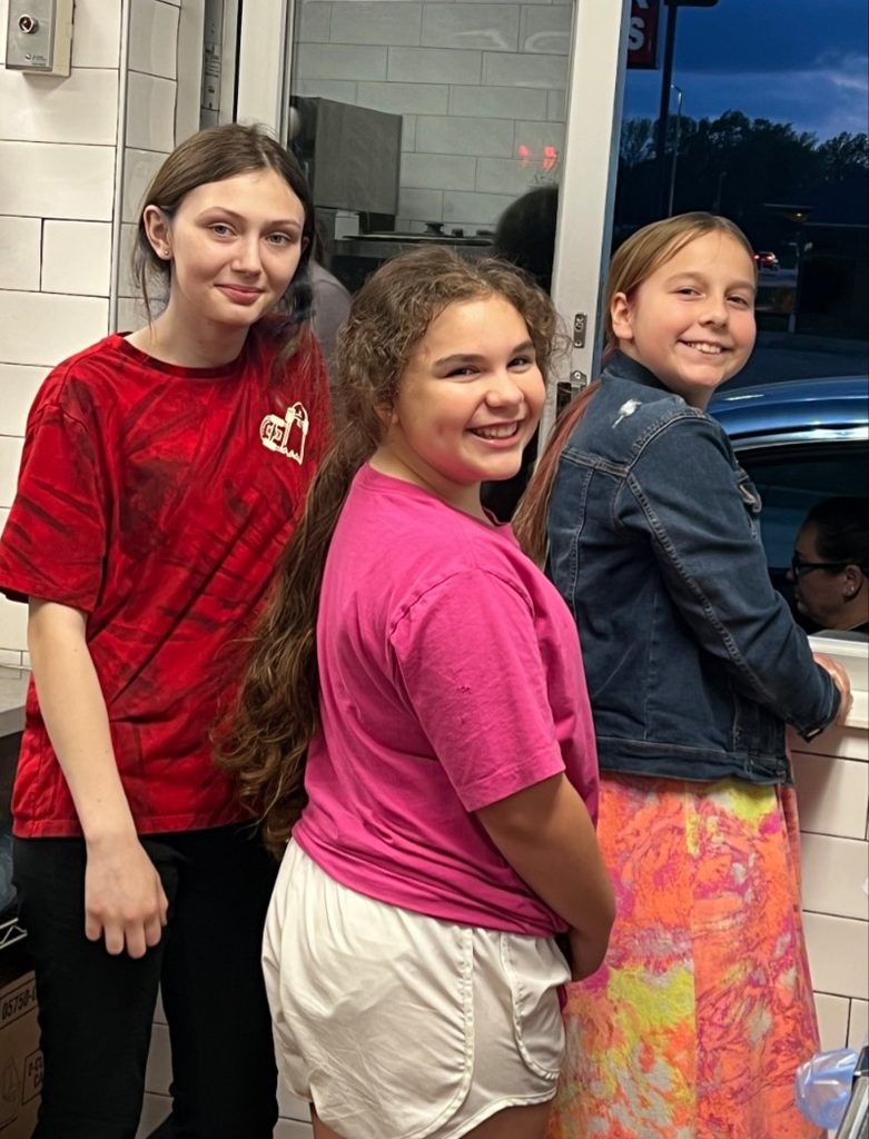 Students smiling and helping at the drive-thru window for Mc Donald's Night.