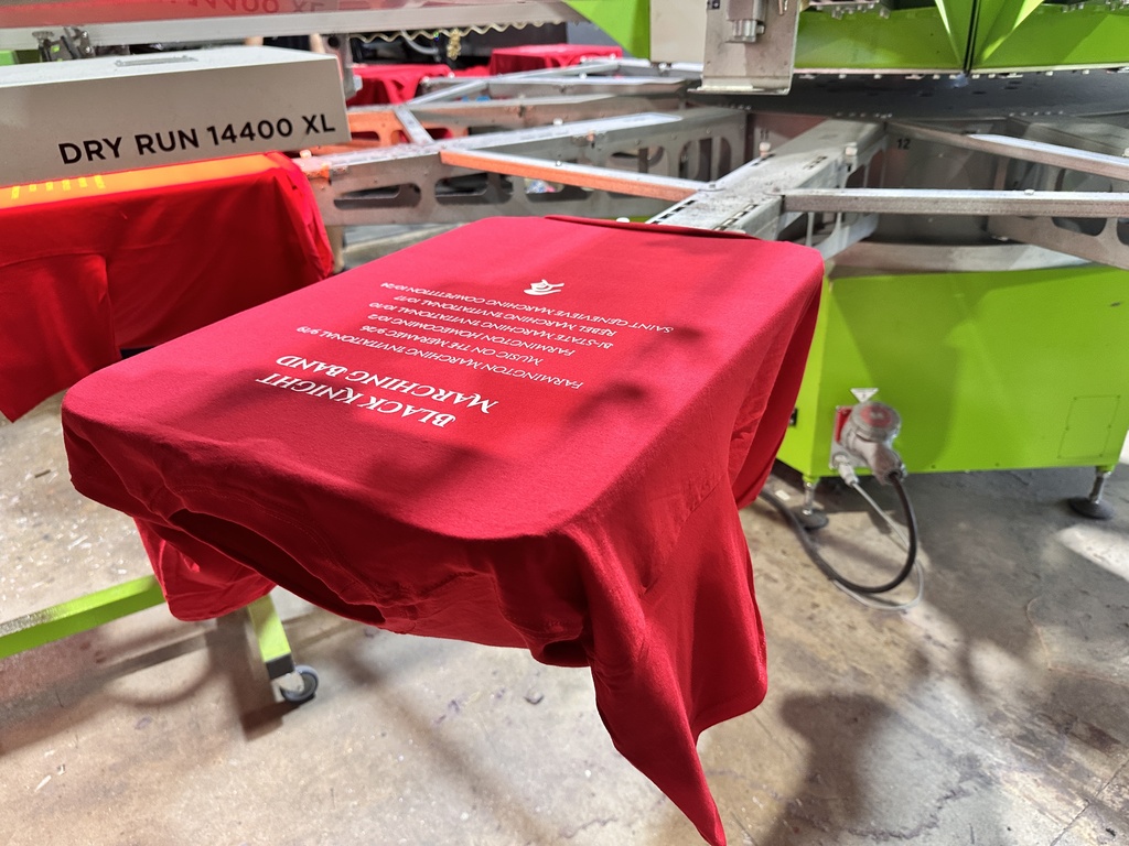 A red cloth placed on a wheeled table, next to a large screen printing machine.