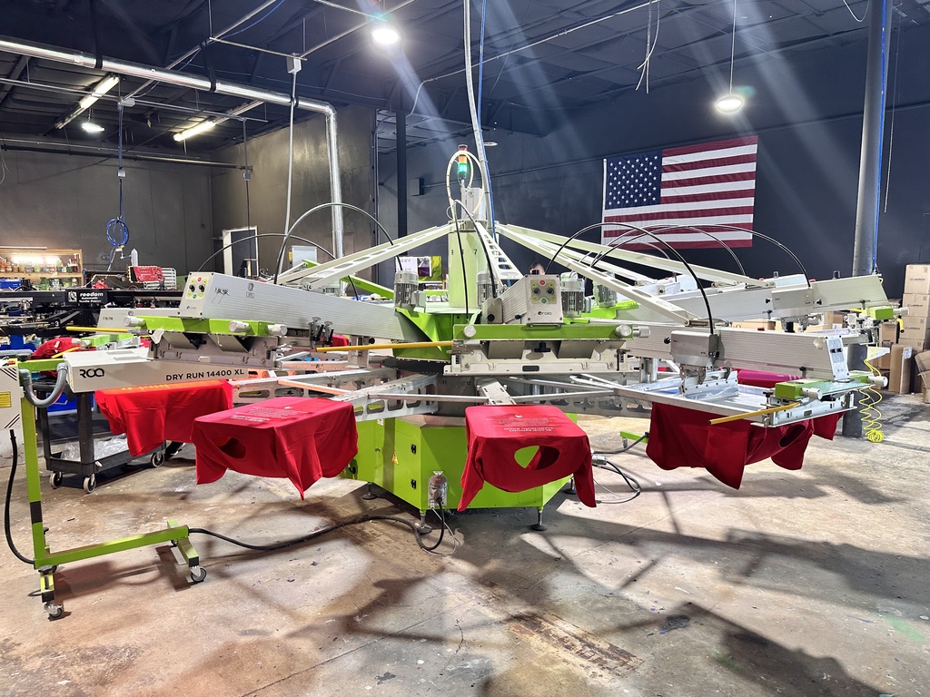 A large industrial machine with red fabric, green frame, and a USA flag in background.