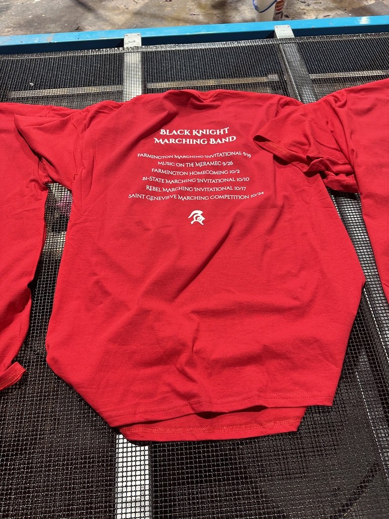 Red shirts with white text on the back are laid out on a black mesh surface.
