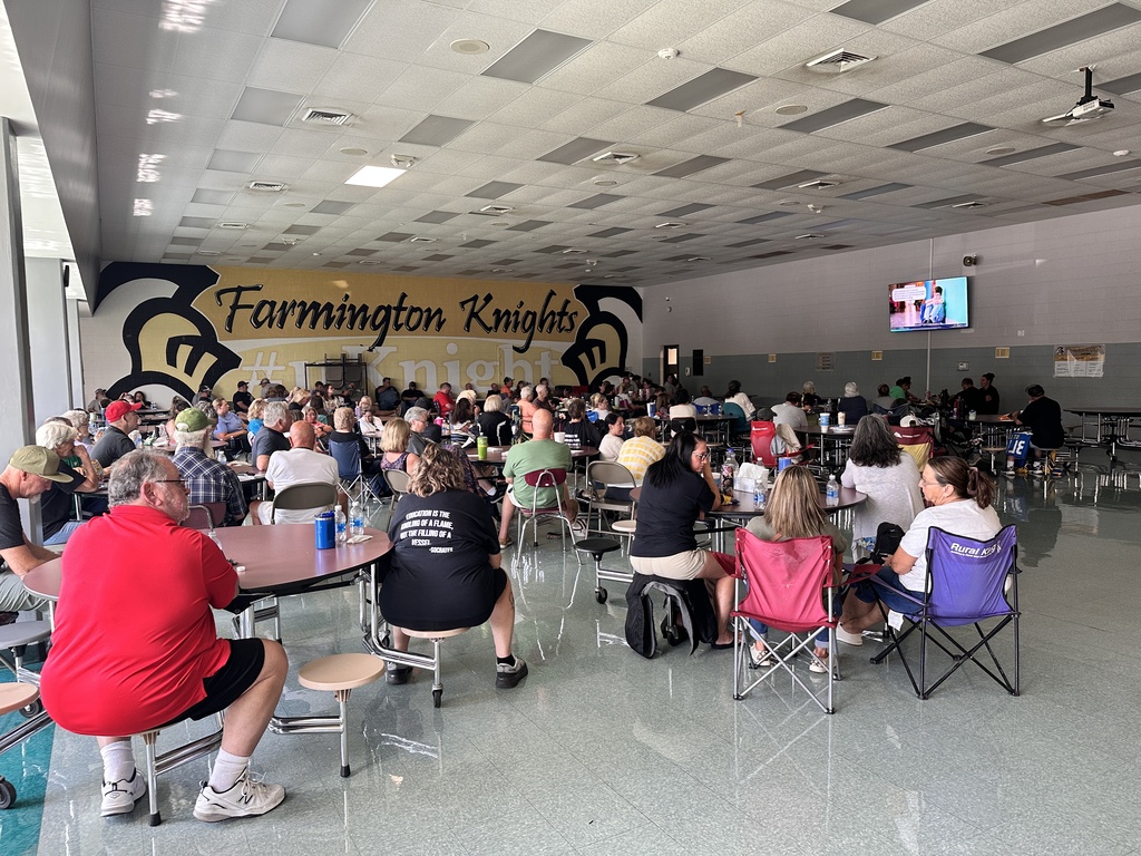 Large indoor room with tables and chairs. A crowd of people sits. A yellow wall displays "Farmington Knights".