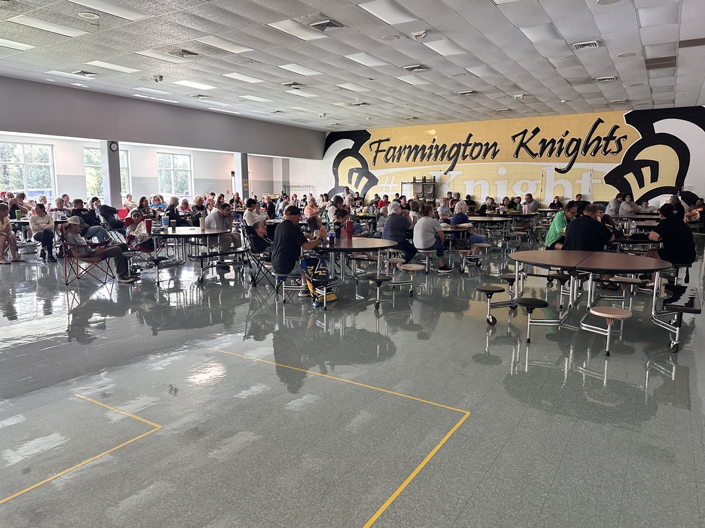 A school cafeteria with many students sitting at tables. A yellow sign reads "Farmington Knights" above the tables.
