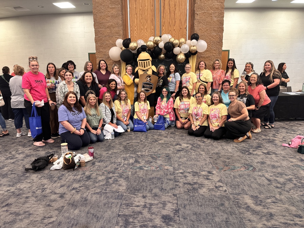 Many women in yellow and pink shirts, posing for a photo, with a mascot and balloons in a large room.