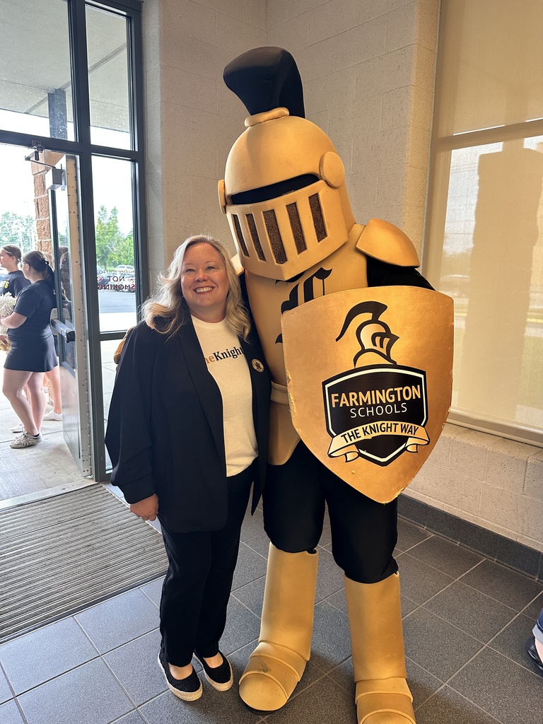 Woman in black and white stands with a golden knight mascot in front of a building.
