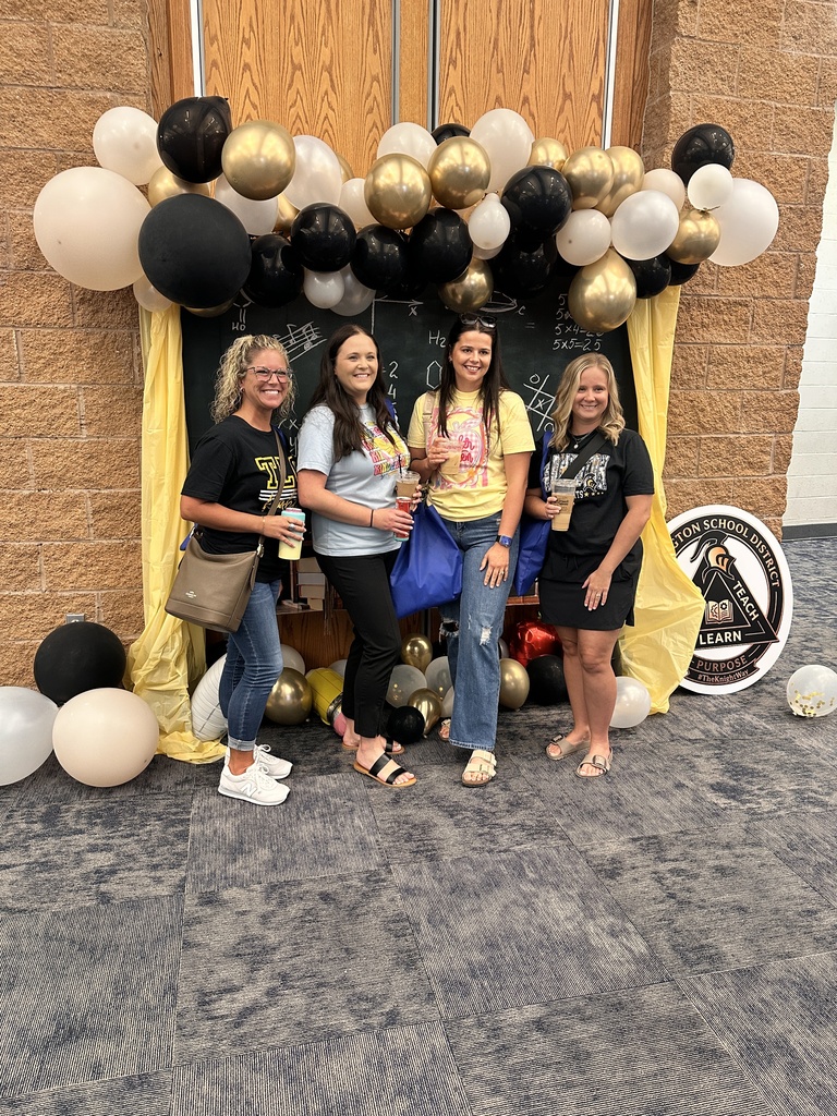 Five women in front of a backdrop with balloons. They are smiling and holding cups.