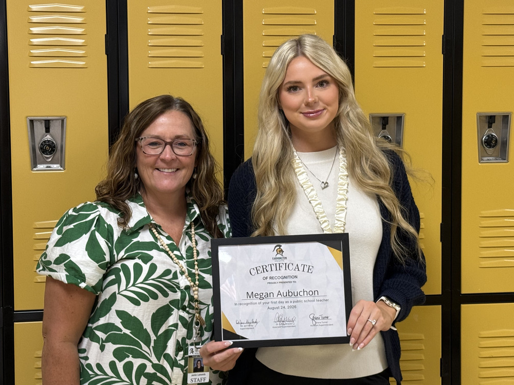 Two women stand in front of lockers. One holds a certificate for Megan Aubchon. Both smile for a photo.