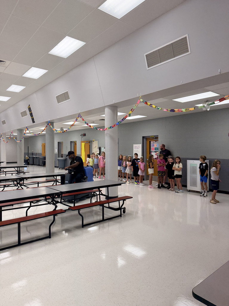 A school cafeteria is empty except for a few children, a man, and a woman. The tables are unoccupied.