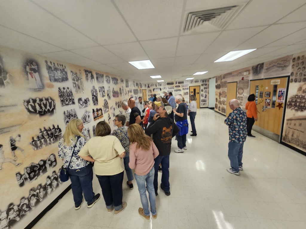 People stand in a hallway with white walls and photographs on the wall, looking at the images.