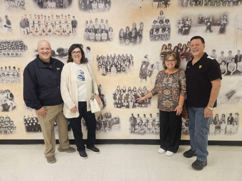 Four people standing in front of a wall with many old photographs. They appear to be smiling.