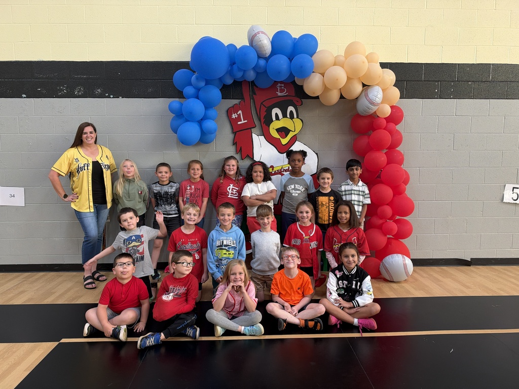 Group of children posing for photo in a gymnasium with an arch of balloons.
