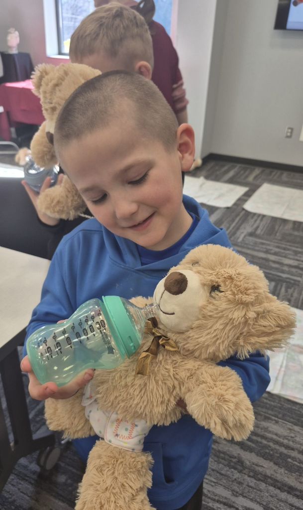 FIRST GRADE BOY FEEDING TEDDY BEAR AT CTE MAGNUS CENTER TEDDY BEAR CLINIC 