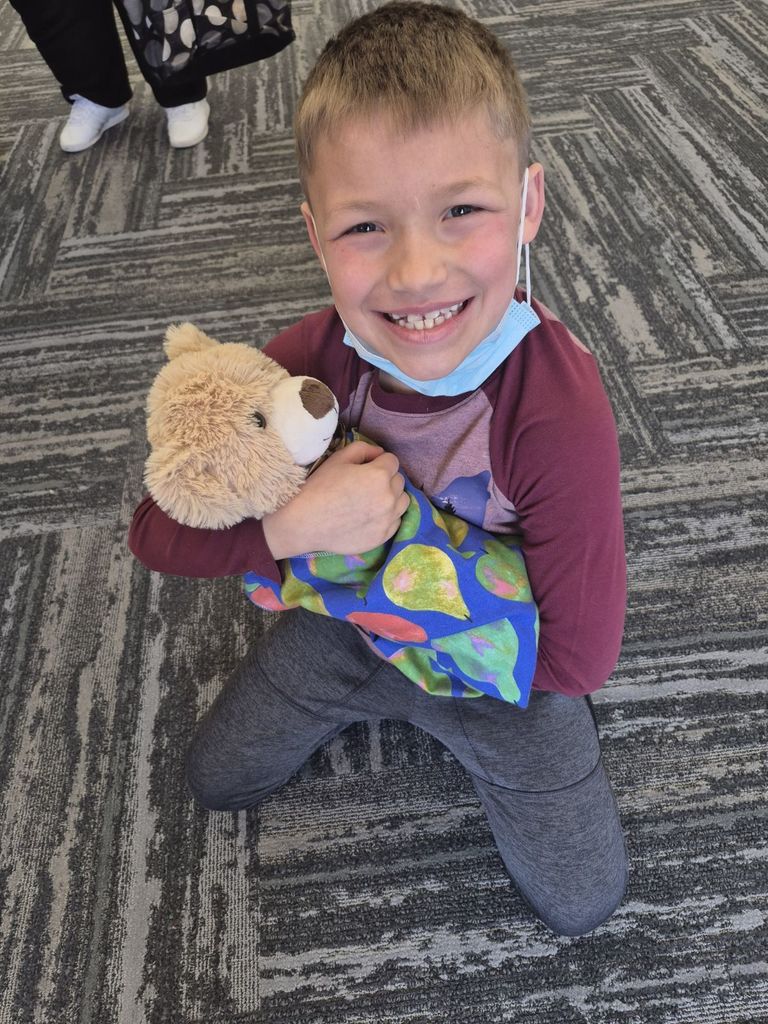 1ST GRADE BOY HOLDING WRAPPED UP TEDDY BEAR AT CTE MAGNUS CENTER TEDDY BEAR CLINIC 