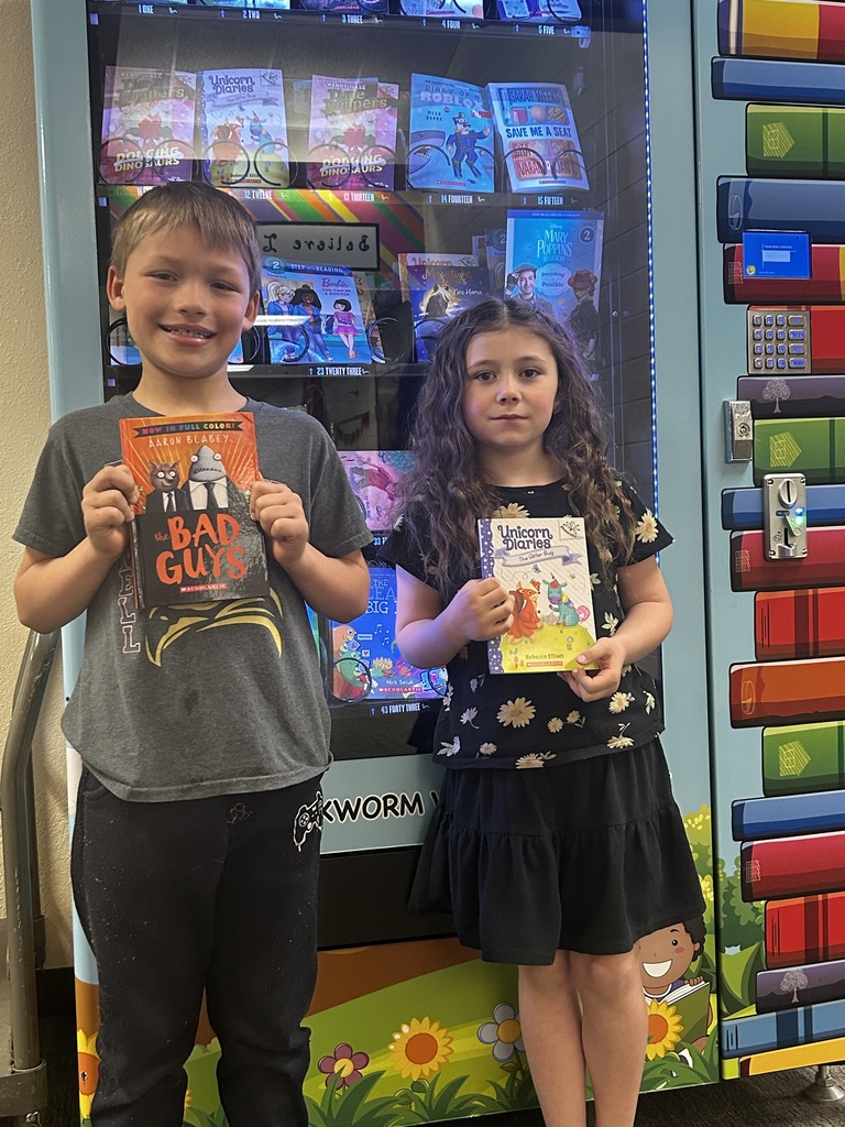 Elementary students holding up books that they received in front of the book vending machine for good behavior. 2026