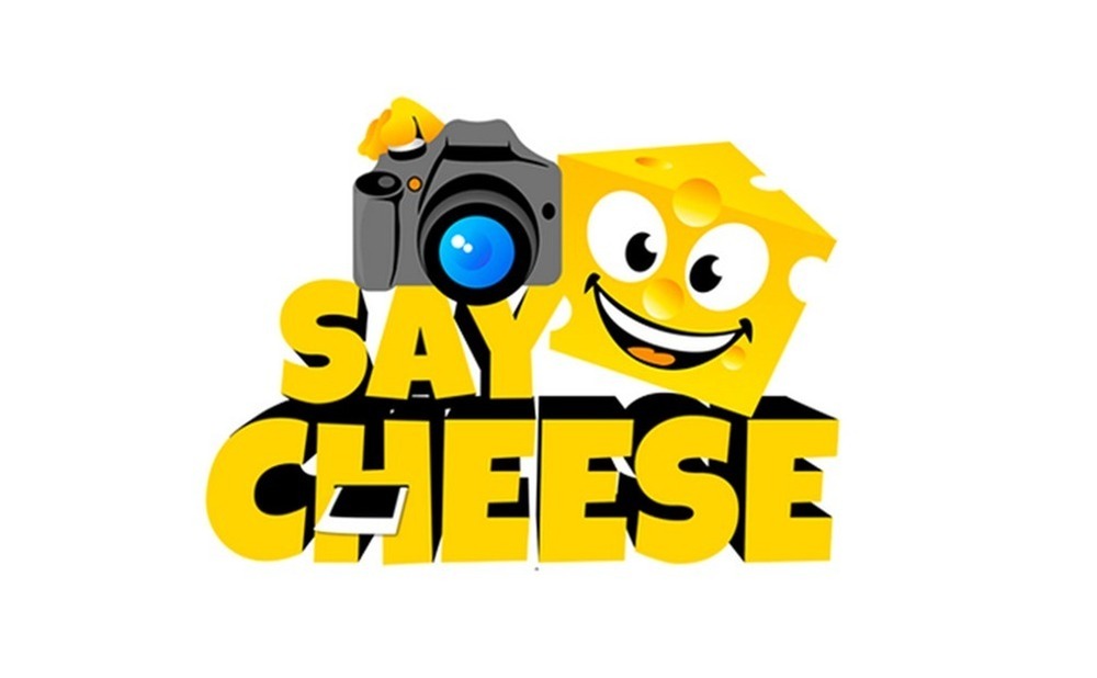 Cartoon piece of cheese with eyes and smile holds camera below cartoon are words SAY CHEESE