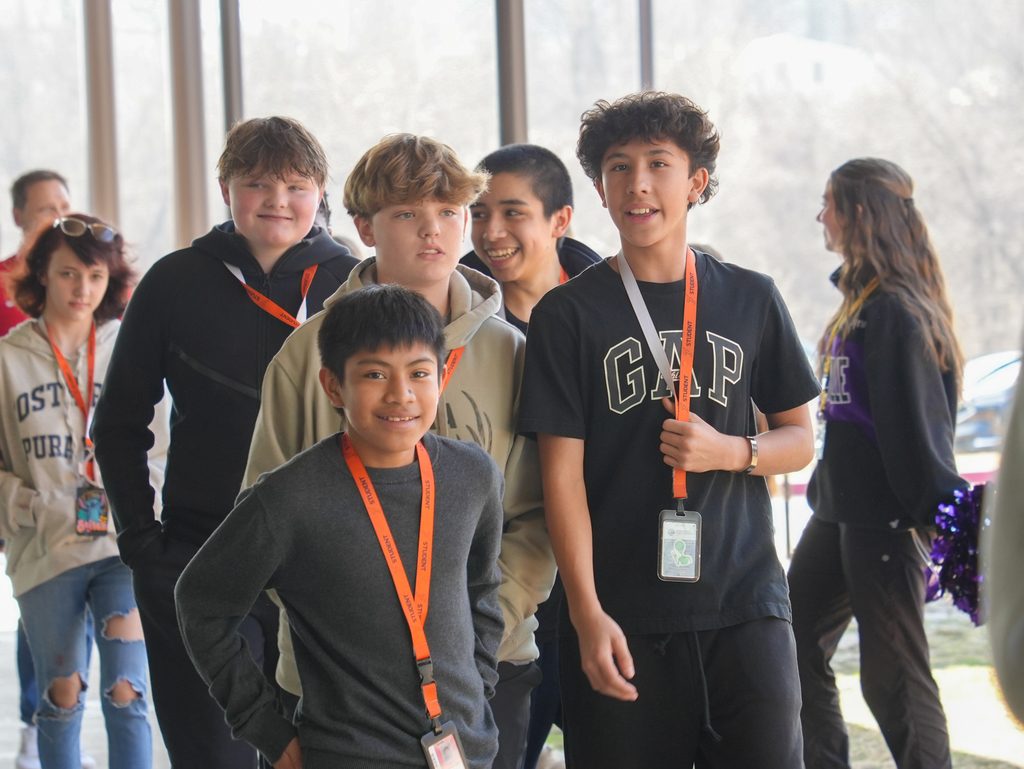 Group of young people wearing orange lanyards, some smiling, in a hallway with glass walls.