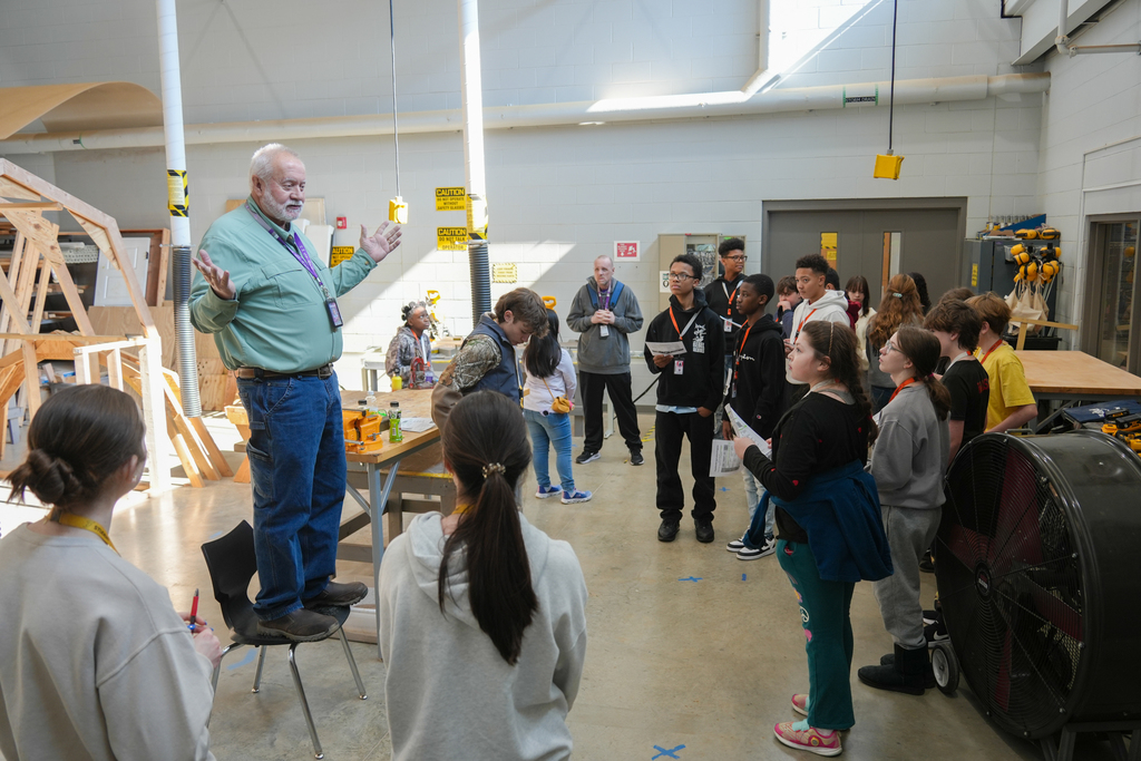 A man in a green shirt leads a discussion with a group of students in a workshop.
